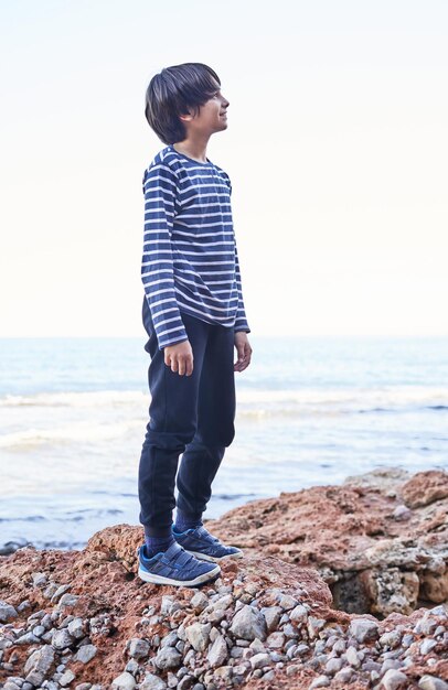 The boy stands on a rock by the sea