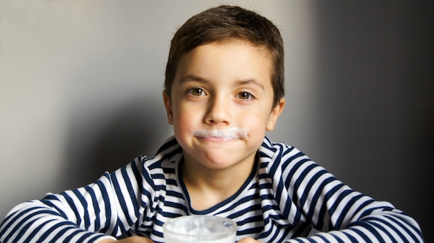 Boy in striped t-shirt with a mustache from kefir or milk with glass in his hand