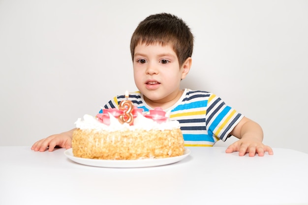 A boy in a striped Tshirt holds a large cake with a candle in the form of the number three