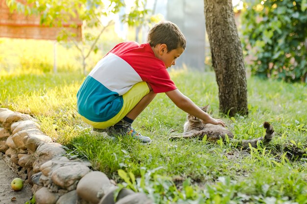 A boy strokes a cat in the yard