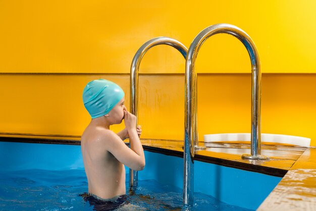 Мальчик плавает в крытом бассейне, развлекаясь во время урока плавания