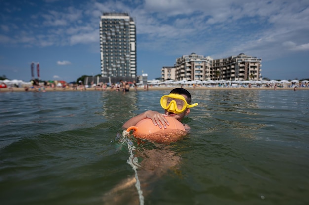 Boy swimming in the sea with orange buoy and diving mask