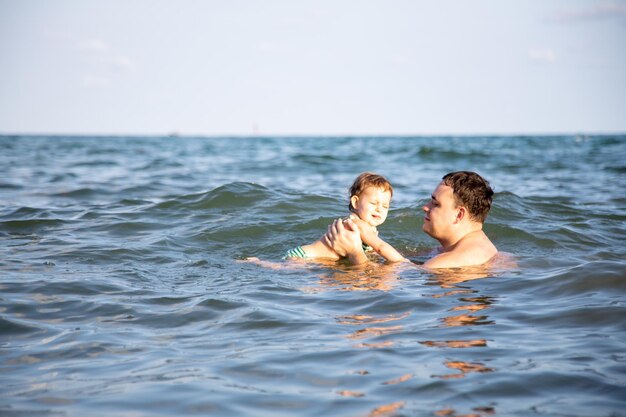 Boy swimming with father in sea against sky