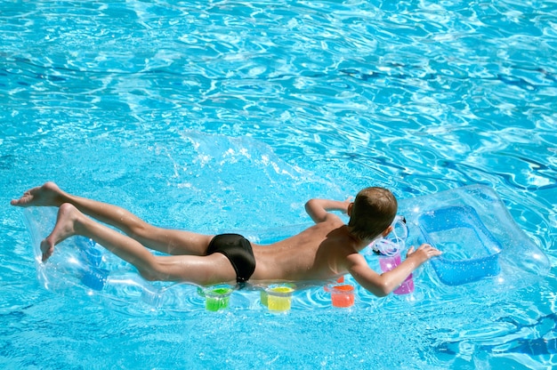 少年は澄んだ水の中の膨脹可能なマットレスで泳ぐ