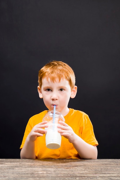 Мальчик за столом пьет коктейль, молочный коктейль, долгожданная еда на заказ, вкусная сладкая еда, портрет крупным планом ребенка мужского пола