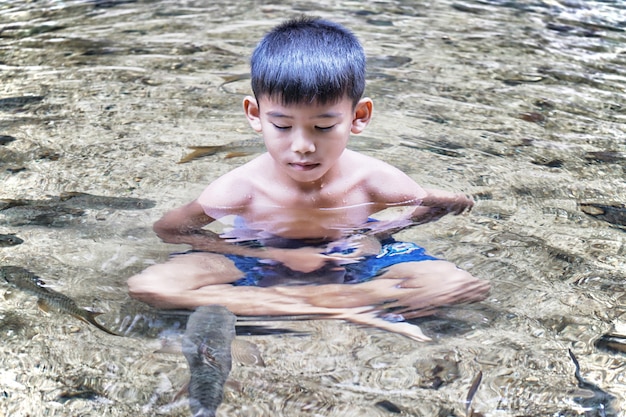 boy take a meditation in the pool and a lot of fish 