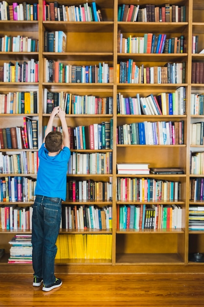 Photo boy taking book from library shelf