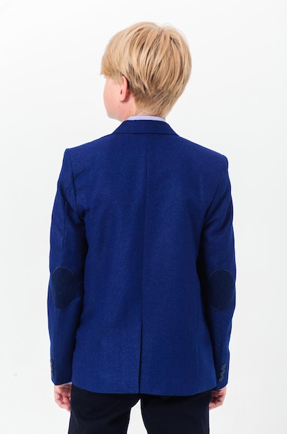 Boy teenager in a school uniform on a white background The schoolboy demonstrates black trousers and a blue jacket from behind from the back Vertical photo