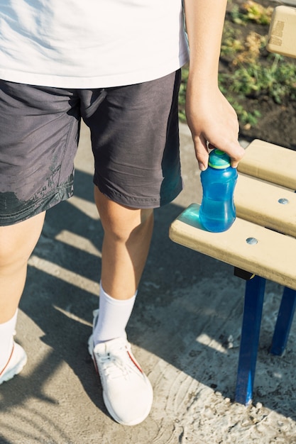 Boy teens working out on the sports ground drinking water from the thermos bottle.