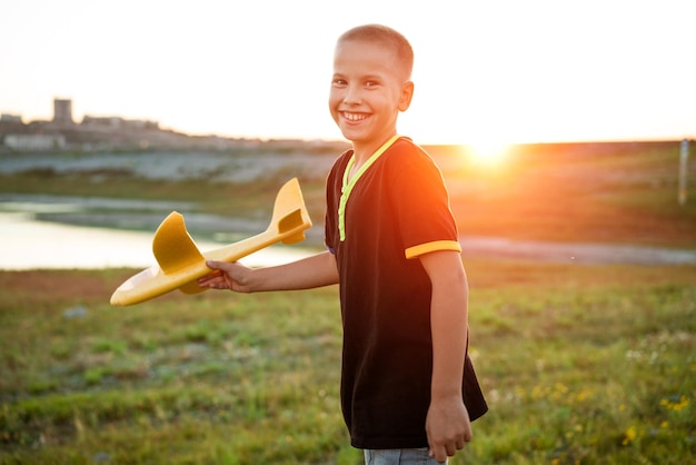 Boy throws a toy airplane in the summer at sunset