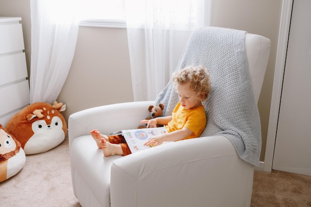 boy toddler 2 years old sitting in armchair reading book early age kid child development education