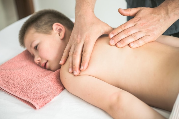 男の子の幼児は、子供の背中を治療するためにクリニックで患者と一緒に働いている治療マッサージ理学療法士からリラックスします