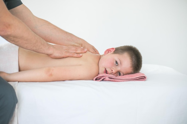 Boy toddler relaxes from a therapeutic massage Physiotherapist working with patient in clinic to treat the back of a child