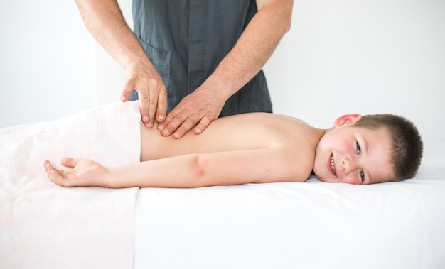 Boy toddler relaxes from a therapeutic massage Physiotherapist working with patient in clinic to treat the back of a child