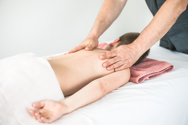 Boy toddler relaxes from a therapeutic massage Physiotherapist working with patient in clinic to treat the back of a child