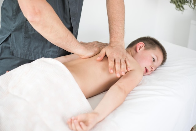 Boy toddler relaxes from a therapeutic massage Physiotherapist working with patient in clinic to treat the back of a child