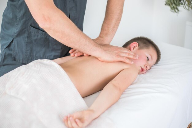 Boy toddler relaxes from a therapeutic massage Physiotherapist working with patient in clinic to treat the back of a child