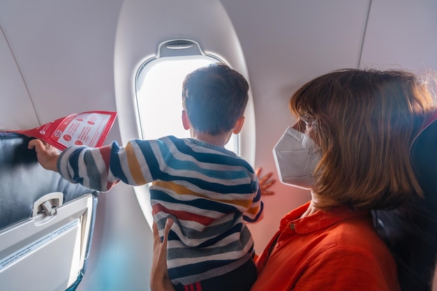 休暇中に飛行機で旅行する少年と母親が窓の外を見て着陸を見ている