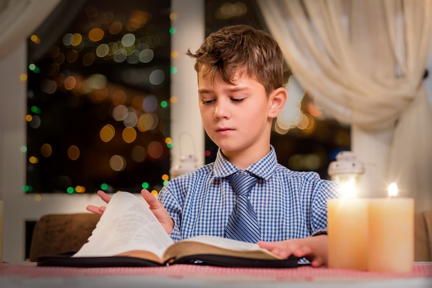 책의 페이지를 넘기는 소년. 촛불로 아이와 책. 그는 절반을 읽었습니다. 시의 거대한 컬렉션.