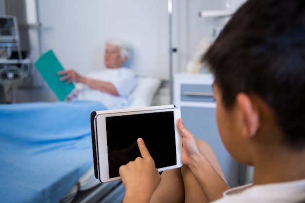 Boy using digital tablet while senior patient reading a book