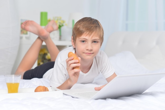 Boy using laptop on bed while having breakfast