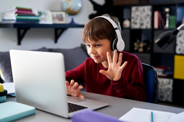 숙제 를 하는 동안 비디오 통화 를 하면서 노트북 을 사용 하고 손을 흔들고 있는 소년