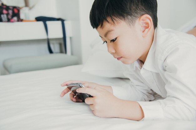 写真 家でベッドで携帯電話を使っている少年