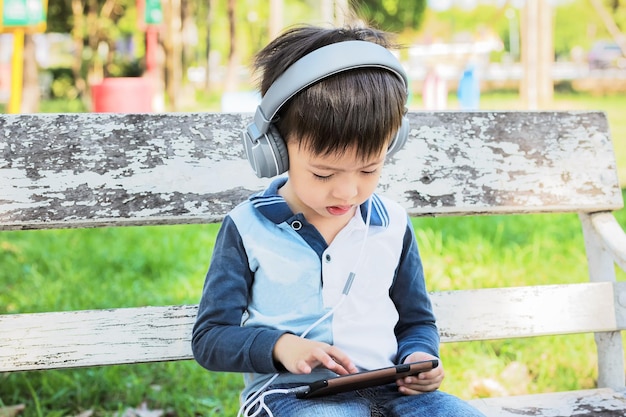 boy using mobile phone while sitting on bench at park