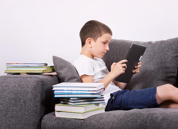 Boy using a tablet PC on the sofa Studio portrait Digital world vs paper book concept