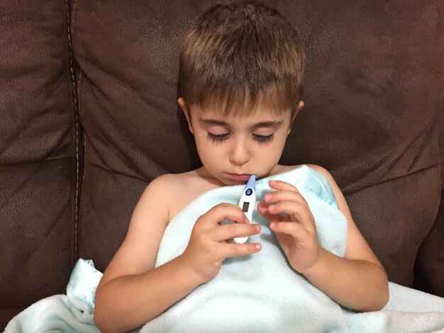 Photo boy using thermometer on sofa at home