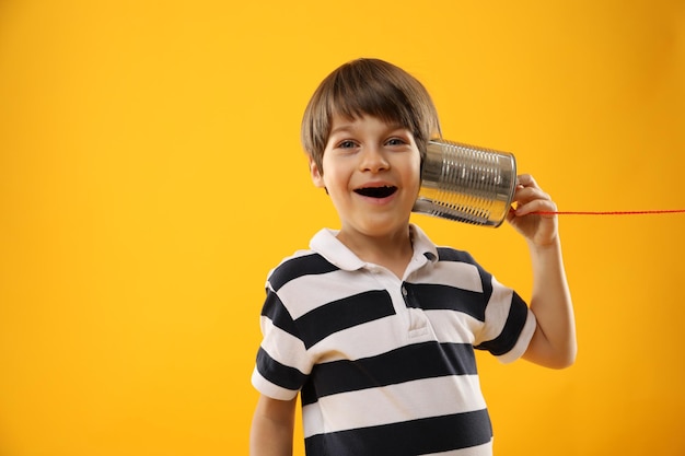 Boy using tin can telephone on yellow background space for text