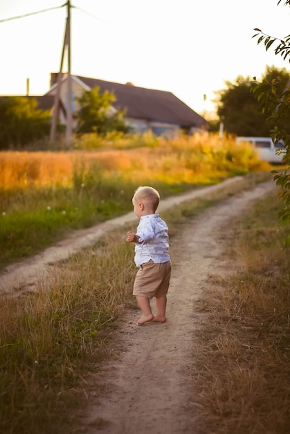 a boy walks along a field road the child smiles green grass a blond boy