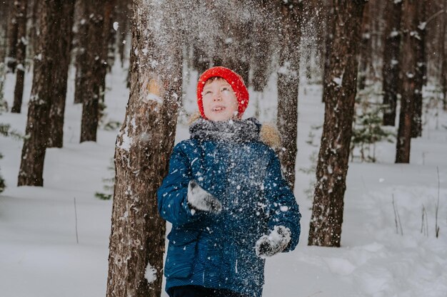 冬の森で雪の中を歩いている少年子供が頭の上に雪を投げかける