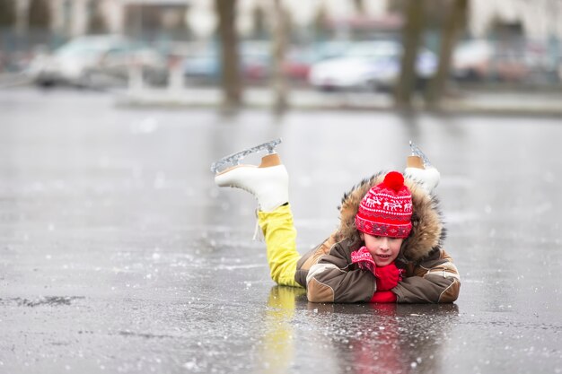 暖かい服とフィギュアスケートの男の子が氷の上に横たわっています。