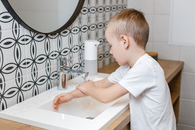 Photo boy washing hands in bathroom using sensor soap dispenser.