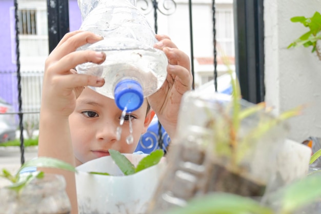 Boy waters his urban garden with plants in recycled plastic bottles from home