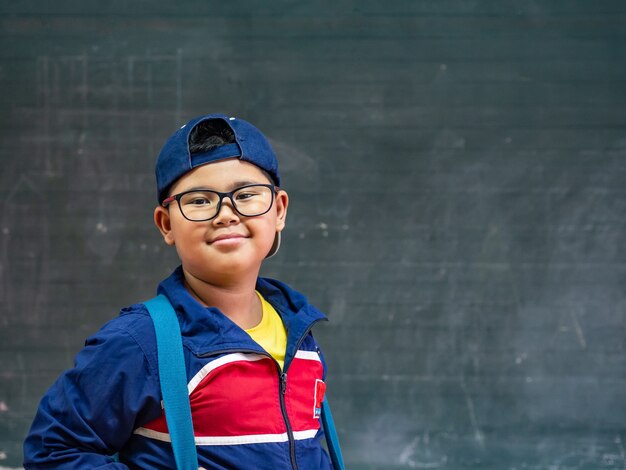 Boy wear glasses smiling and stand in front of the blackboard. Back to School.