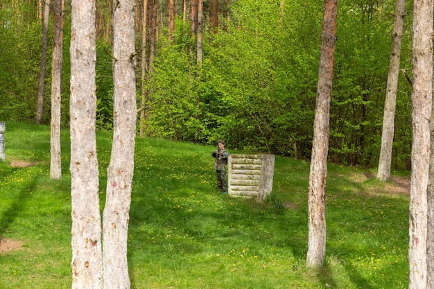 Мальчик в камуфляже играет в лазертаг на специальной лесной площадке