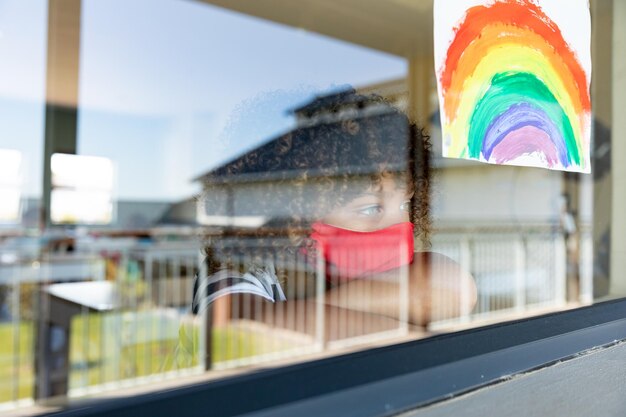 Foto ragazzo che indossa una maschera facciale che guarda fuori dalla finestra