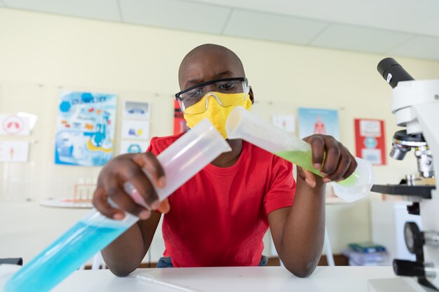 Boy wearing face mask and protective glasses mixing chemicals in laboratory