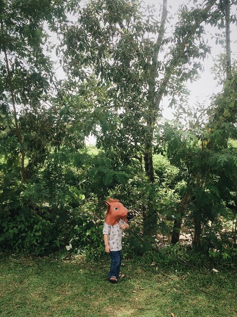 Photo boy wearing horse mask while standing against trees