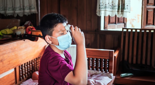 boy wearing a mask use the temperature taken for the scan of fever with an infrared thermometer