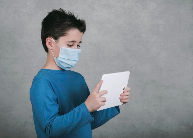 Boy wearing mask using digital tablet against gray background