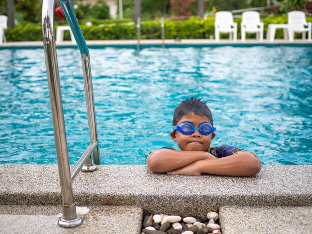 The boy wearing swimsuits and glasses Smile while perched on the edge of the swimming pool