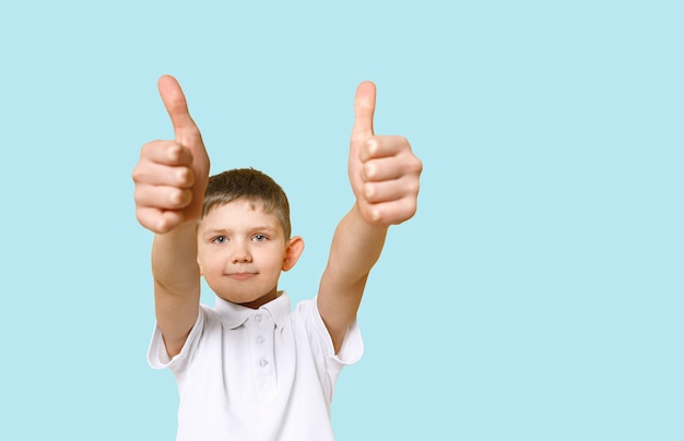 Boy wearing white t-shirt showing thumbs up, portrain on light blue background.