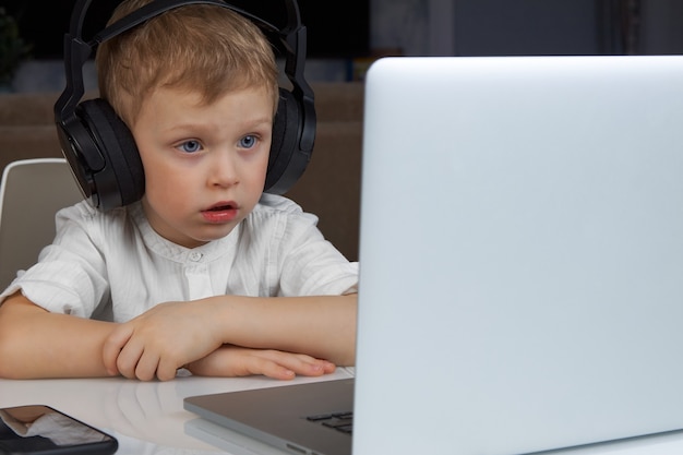 Boy wearing wireless headphones sitting at a desk using a laptop