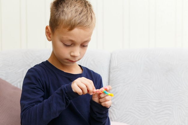 Boy weaves bracelet of rubber rings at home on the couch