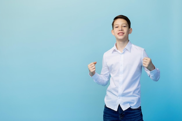 Boy in a white shirt and jeans rejoices on a plain blue background and smiles