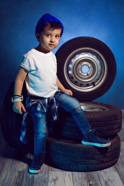 白いTシャツシャツと帽子を着た少年が ⁇ 青色の車輪の背景に座っています ⁇