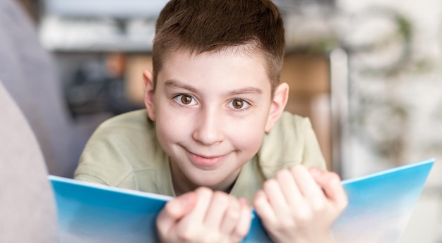 Photo boy in white tshirt looking at camera while sitting in sofa with book